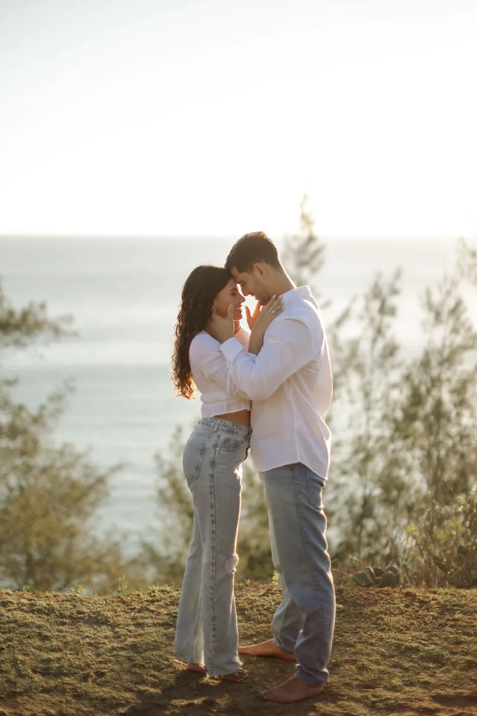 Casal testa com testa na beira do penhasco, com o mar atrás