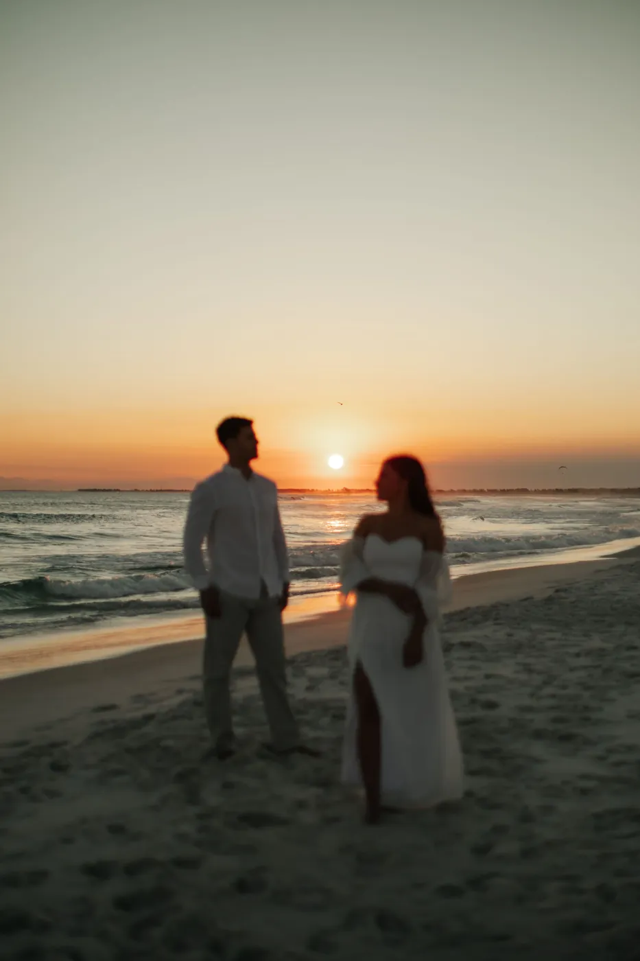 Silhuetas do casal na praia, com o sol se pondo entre os dois