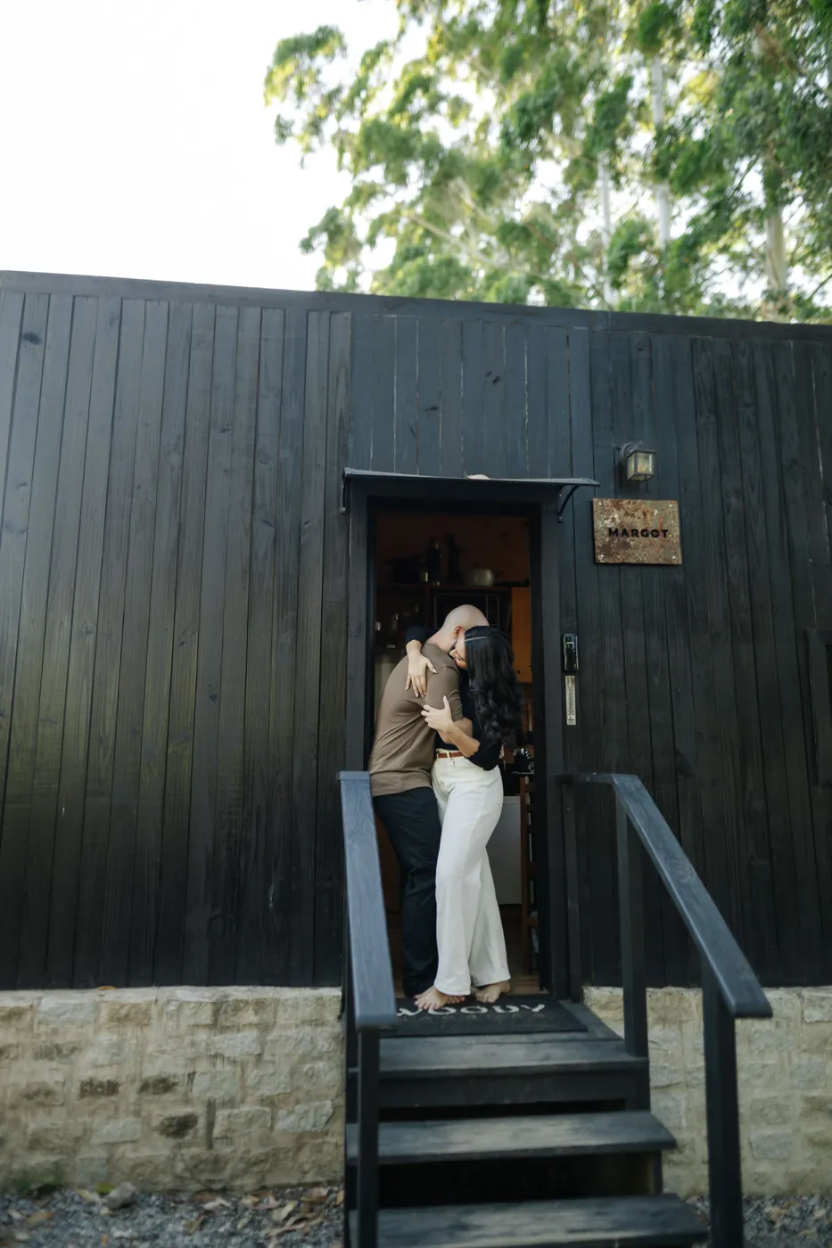 Casal se abraçando na porta da cabana de madeira escura