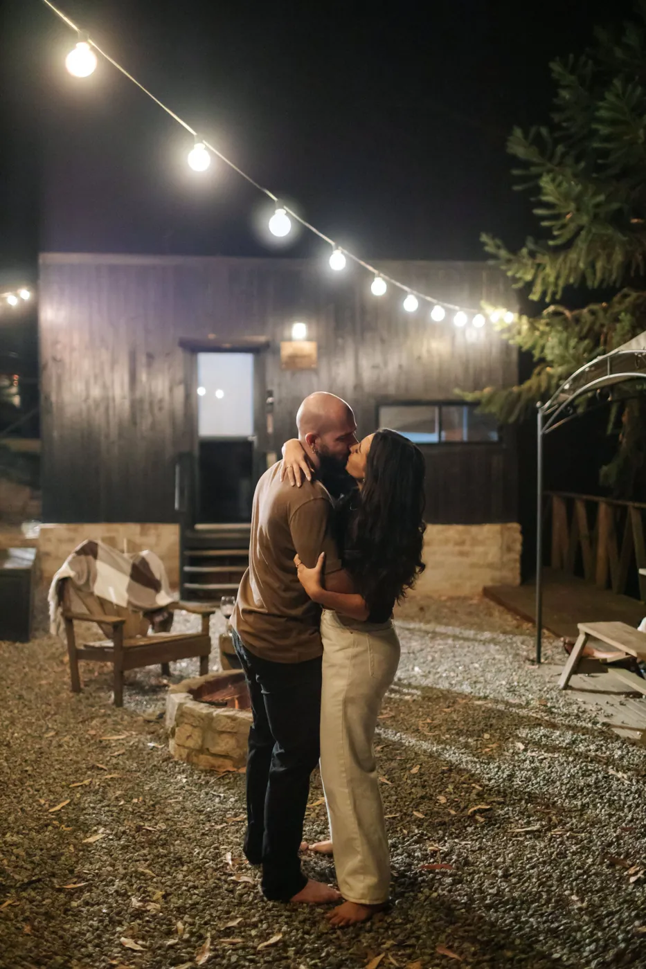Casal se beijando sob as luzinhas, com a cabana ao fundo