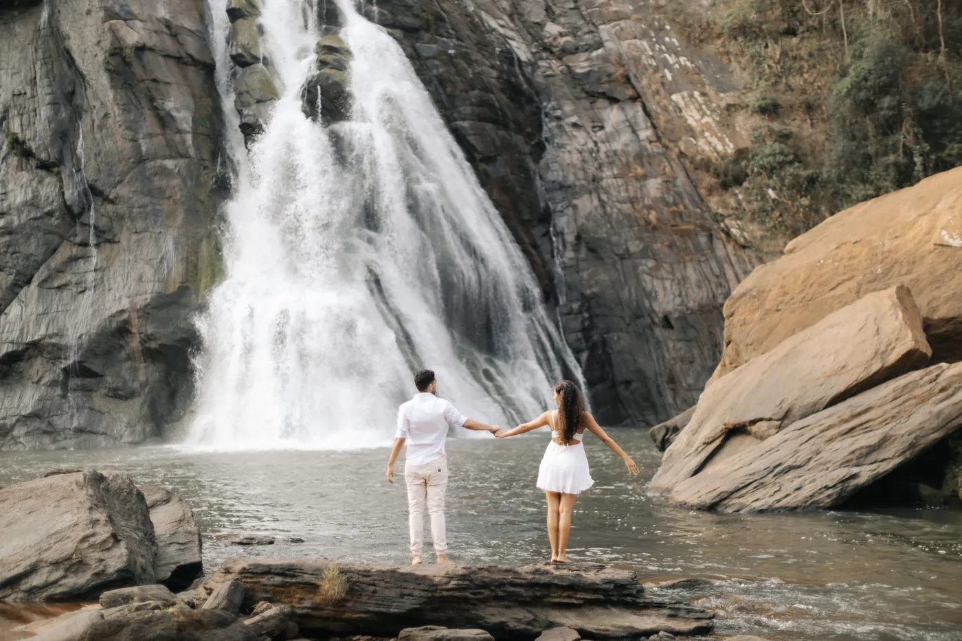 Casal de mãos dadas de costas, olhando a cachoeira