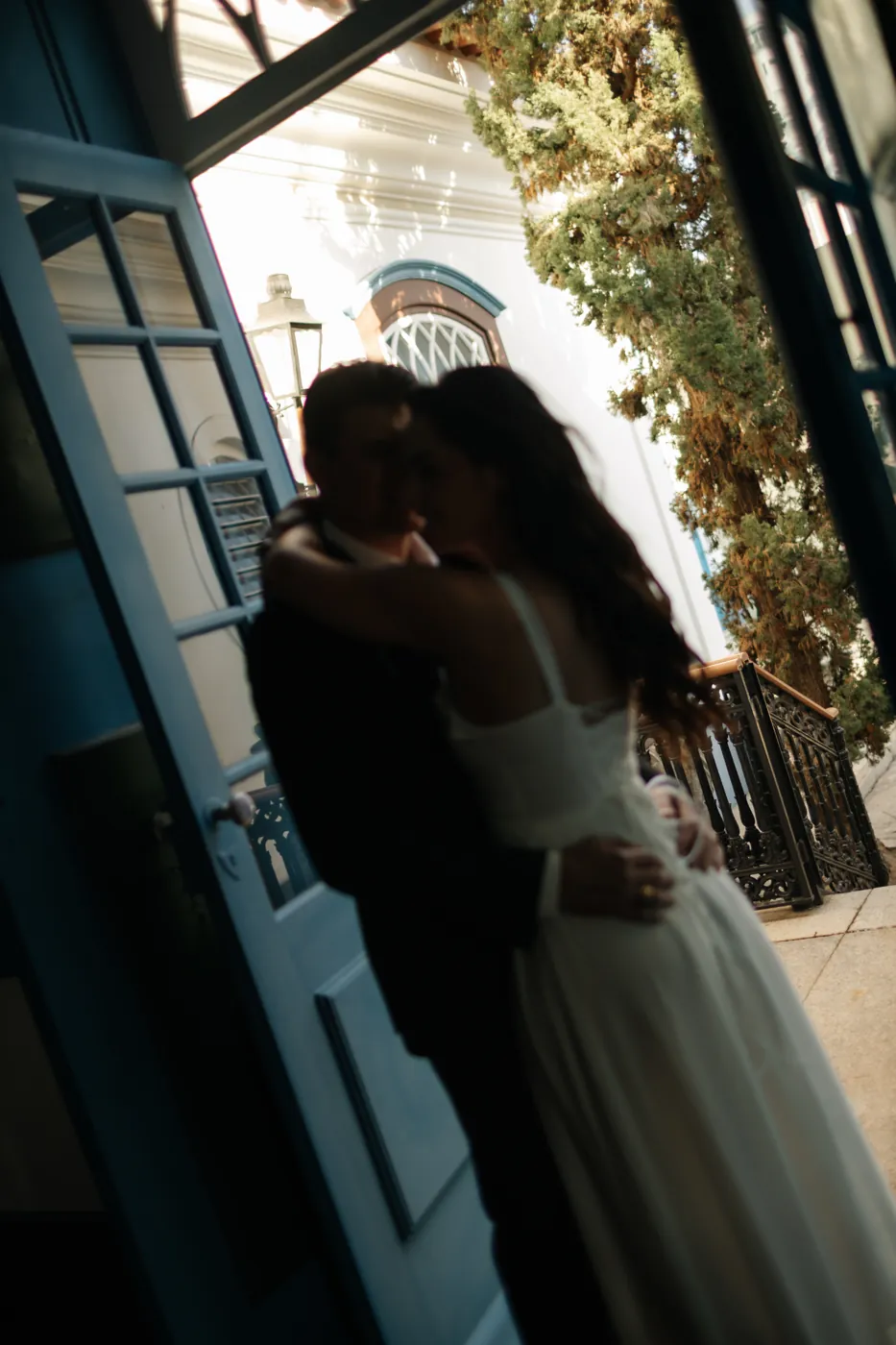Casal abraçado visto de dentro, pela porta azul, em contraluz