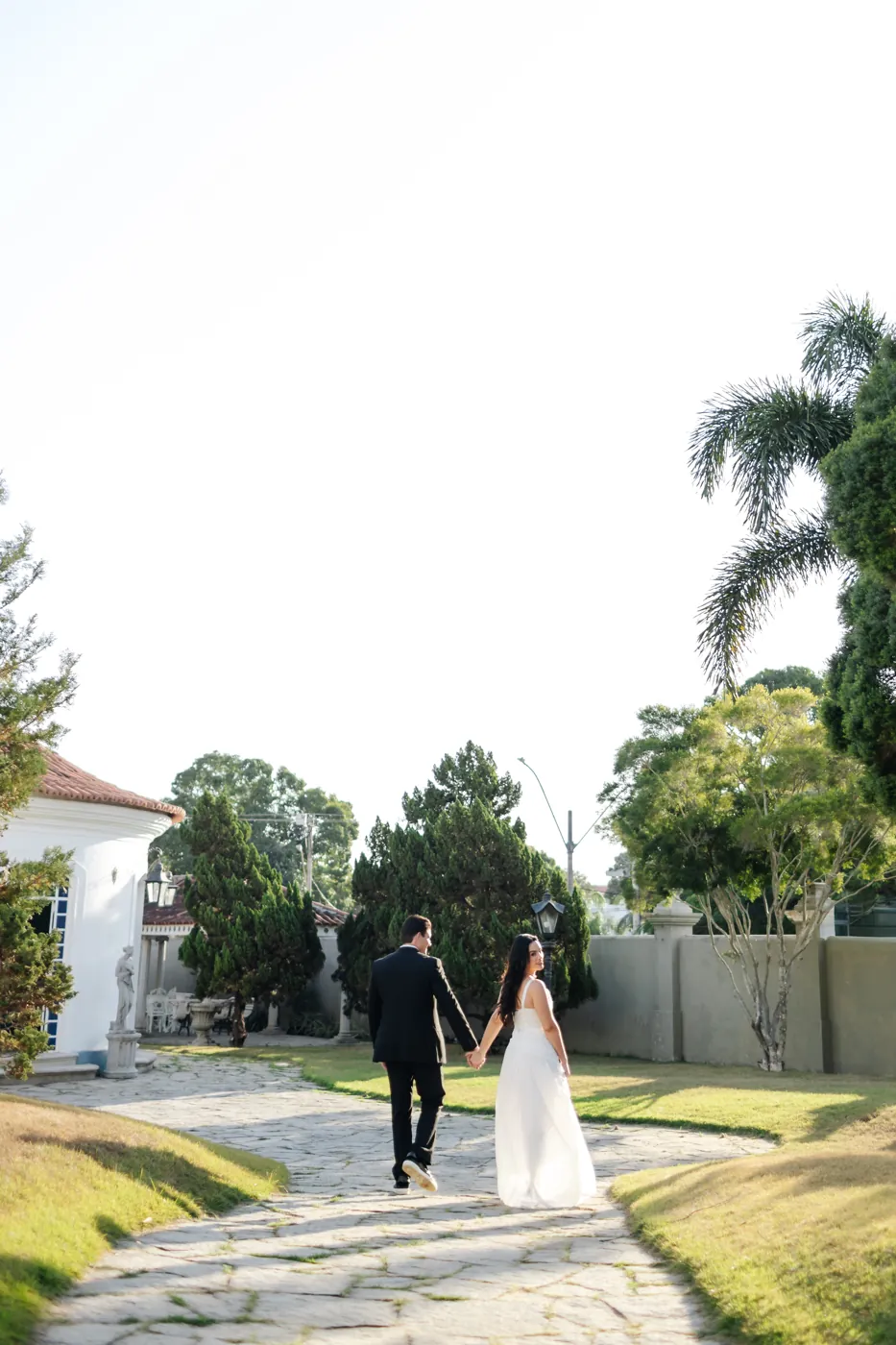 Casal de mãos dadas caminhando pelo jardim, ela olhando para trás