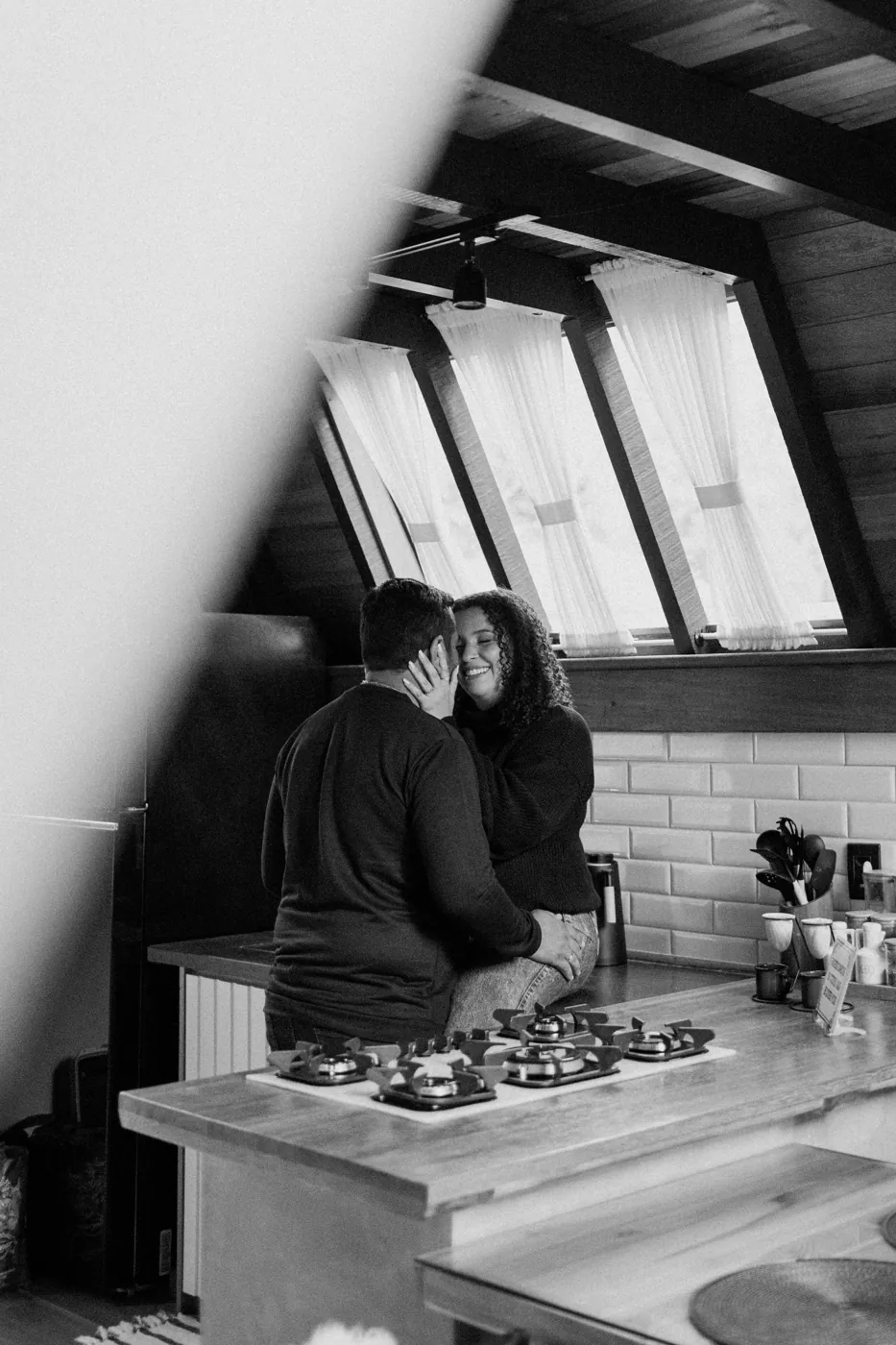 Casal na bancada da cozinha do chalé, em preto e branco