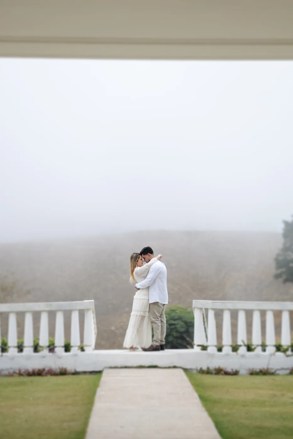 Casal abraçado no mirante, com a neblina cobrindo o vale