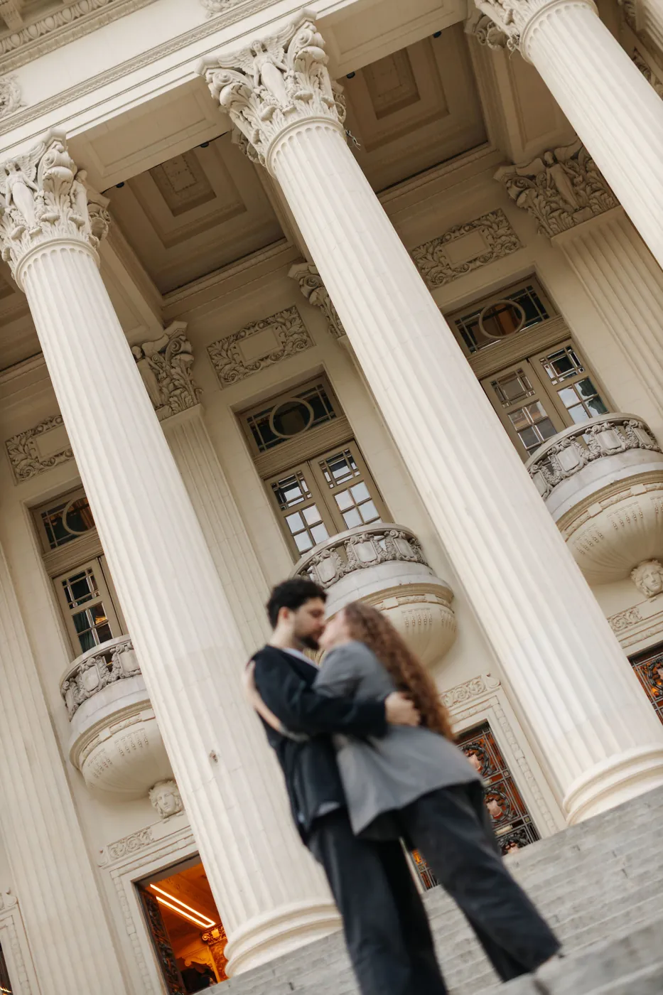 Casal se beijando na escadaria de um prédio histórico de colunas