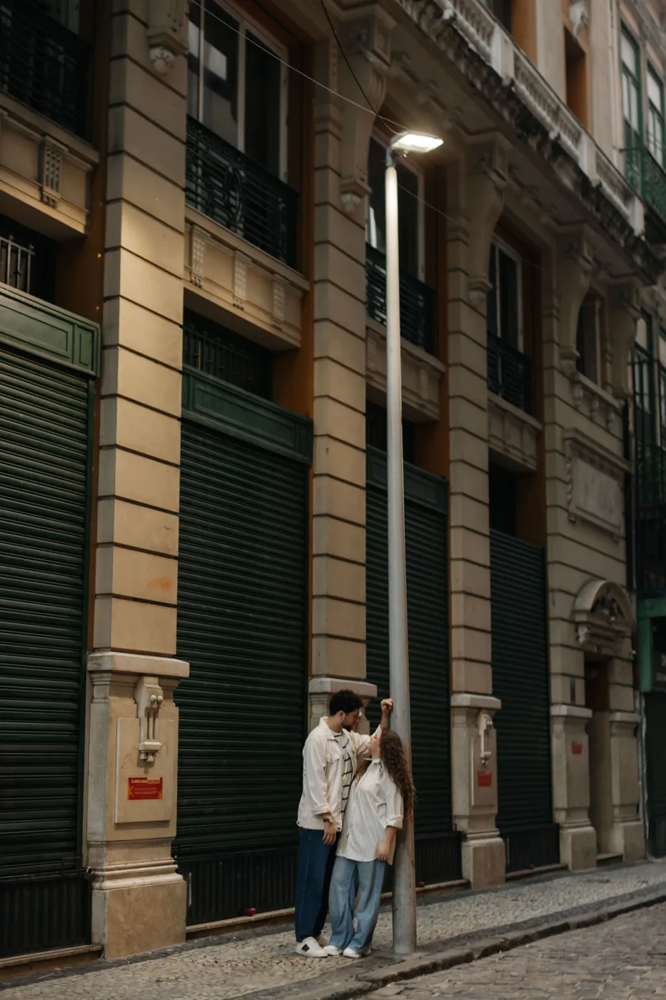 Casal encostado num poste numa rua de fachadas antigas