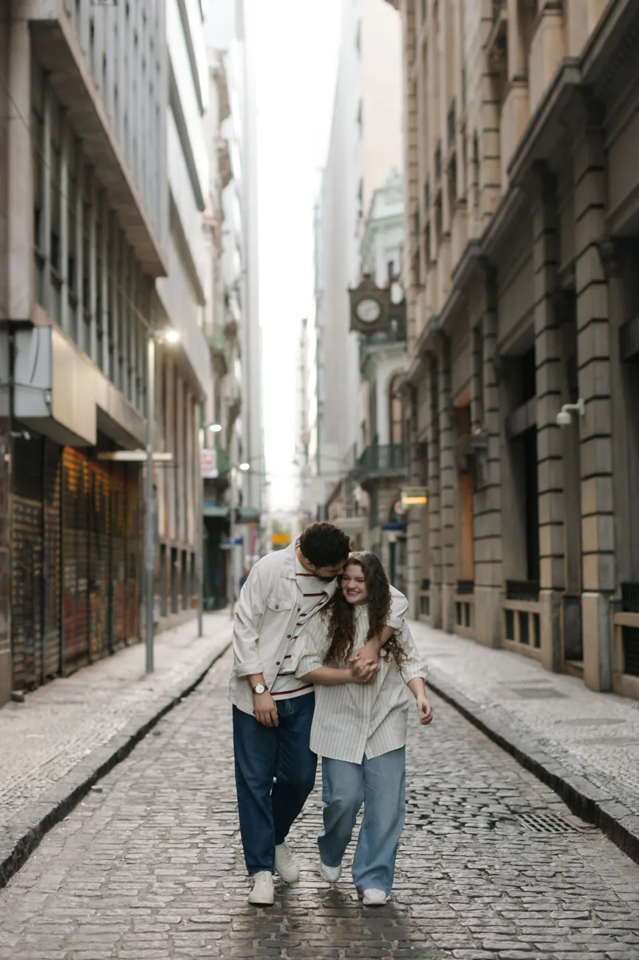 Casal abraçado rindo, caminhando numa rua de paralelepípedos