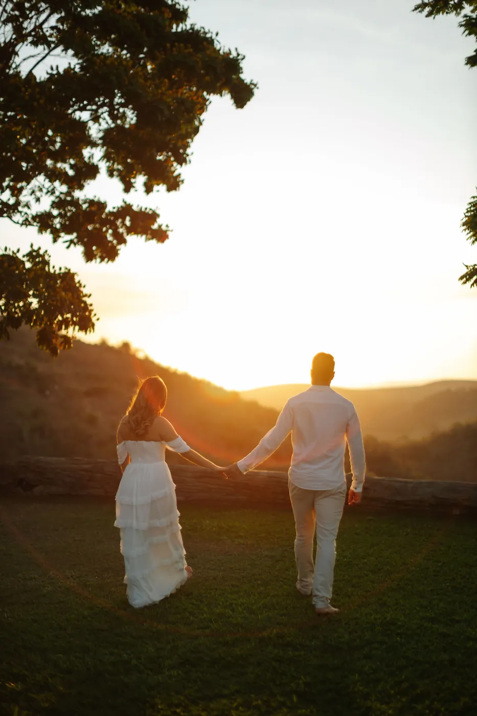 Casal de mãos dadas caminhando no gramado em direção ao pôr do sol